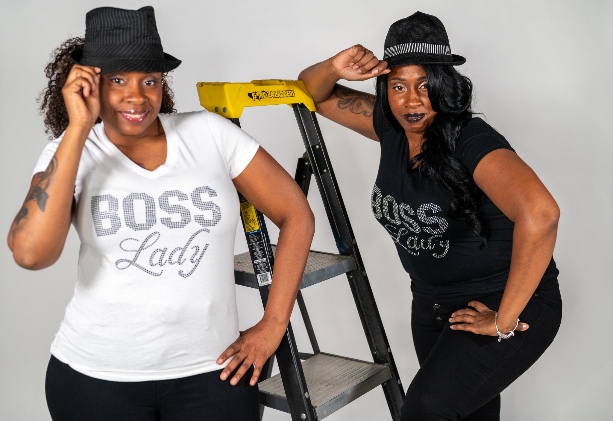 Tracey and Stacey L posing beside a ladder in coordinated Boss Lady outfits